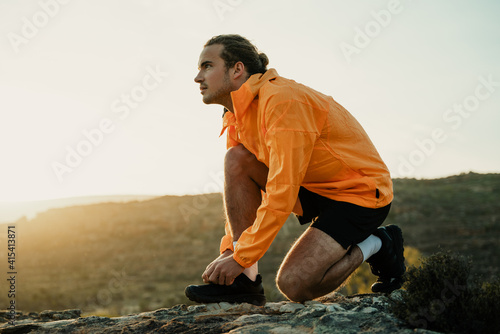 Bilde på lerret Caucasian male athlete taking a break from run tying shoe lace while hiking in m