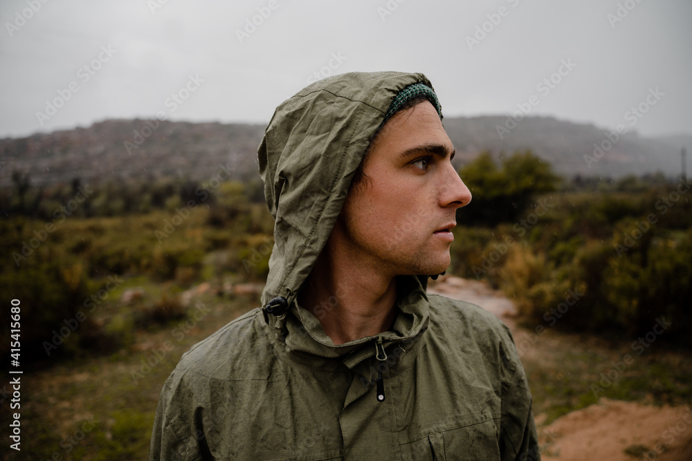 Young fit male athlete resting while concentrating on gravel mountain path ahead with bushes and hills behind him Young fit male athlete resting while concentrating on gravel mountain path ahead with bushes and hills behind him
