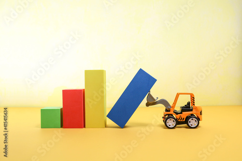 A toy bulldozer holding the blue pilon from falling 