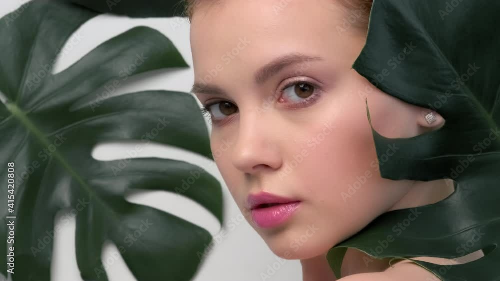 Closeup face of young beautiful woman with a healthy clean skin. Beautiful white girl with big green leaves. Beauty and spa treatment concept. Pretty woman with natural makeup and plant near face. Closeup face of young beautiful woman with a healthy clean skin. Beautiful white girl with big green leaves. Beauty and spa treatment concept. Pretty woman with natural makeup and plant near face.
