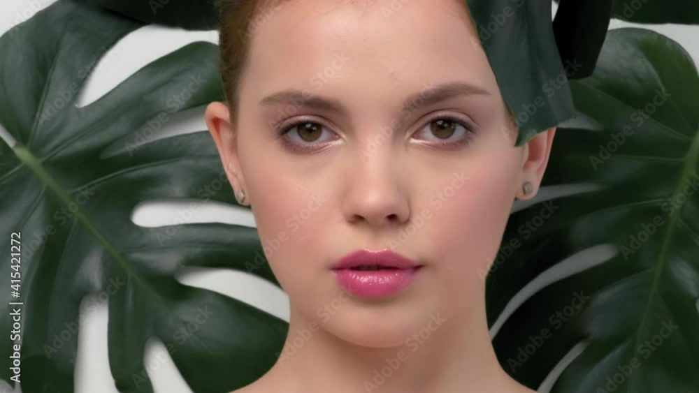 Closeup face of young beautiful woman with a healthy clean skin. Beautiful white girl with big green leaves. Beauty and spa treatment concept. Pretty woman with natural makeup and plant near face. Closeup face of young beautiful woman with a healthy clean skin. Beautiful white girl with big green leaves. Beauty and spa treatment concept. Pretty woman with natural makeup and plant near face.