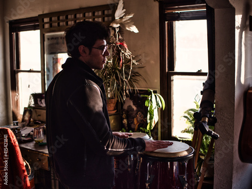 Wallpaper Mural Side view of young guy in stylish jacket and glasses playing bongo drums and looking away in cozy retro room Torontodigital.ca