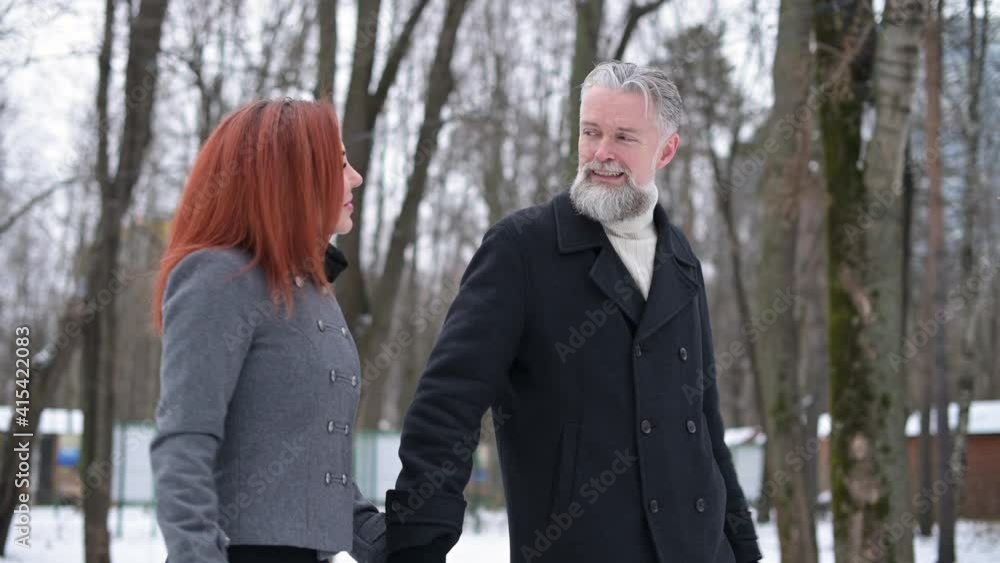 A close-up of a gray-haired man walking and chatting with a young woman. A date in the park on a winter day A close-up of a gray-haired man walking and chatting with a young woman. A date in the park on a winter day