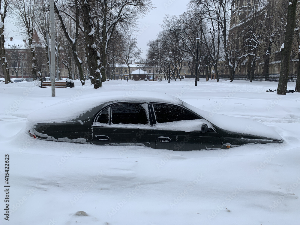 The car was covered with snow in the parking lot. Cars under a large layer of snow. Snowfall on the streets of Europe. The car was covered with snow in the parking lot. Cars under a large layer of snow. Snowfall on the streets of Europe.