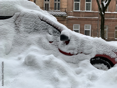 The car was covered with snow in the parking lot. Cars under a large layer of snow. Snowfall on the streets of Europe.