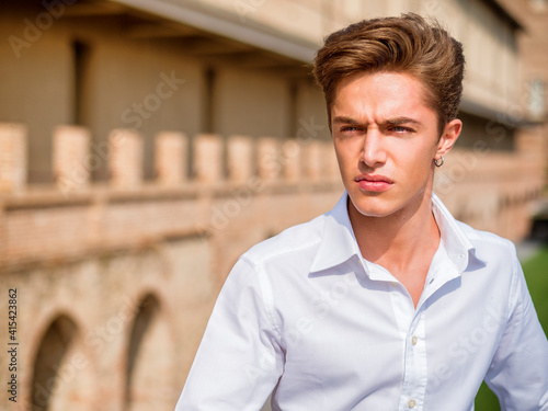 One handsome elegant young man in urban setting in European city, standing in sunny day