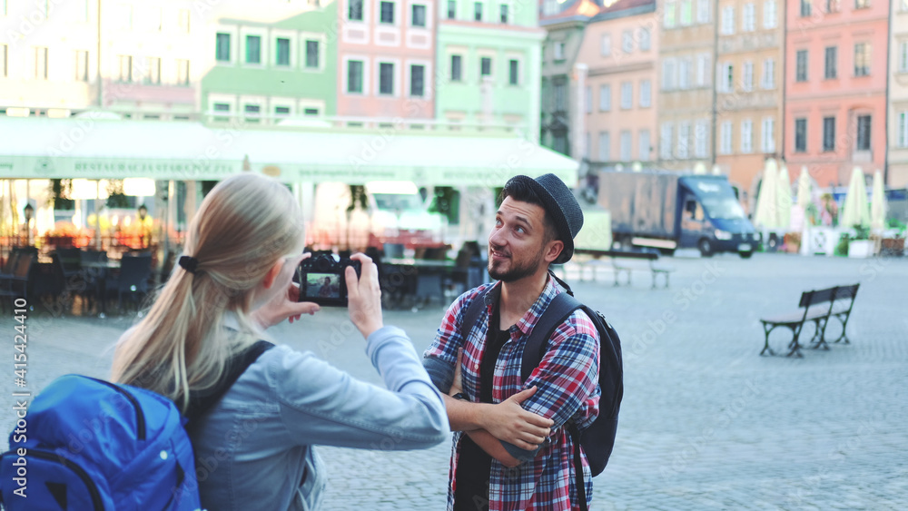 Medium shot of couple of tourists making photos with photo camera on historical market square. Man posing and woman taking photos.