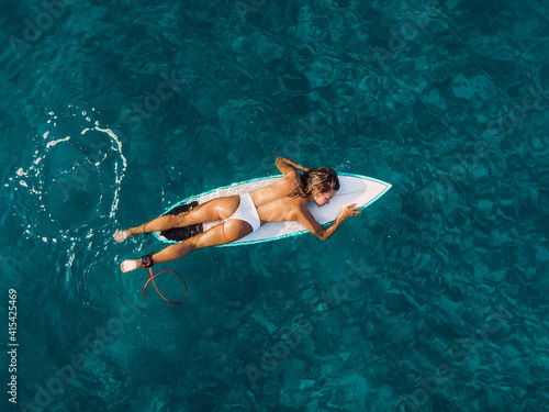 Attractive surfer woman relaxing on surfboard in ocean. Aerial view with surf girl