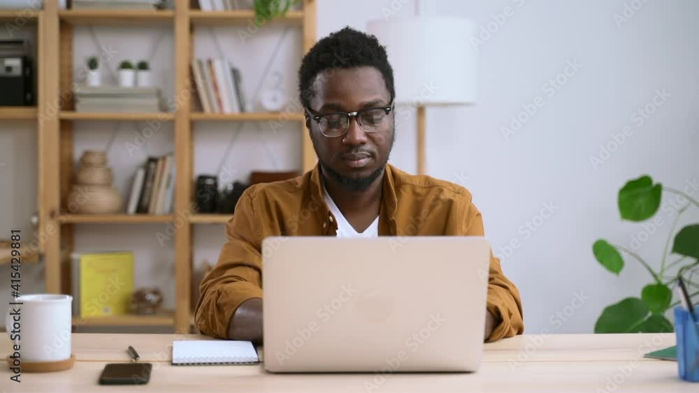 African business man sit in home office, using laptop, think about idea and plan for work distantly. Spbas. Guy freelancer type on computer. Concept glasses, internet, thought African business man sit in home office, using laptop, think about idea and plan for work distantly. Spbas. Guy freelancer type on computer. Concept glasses, internet, thought