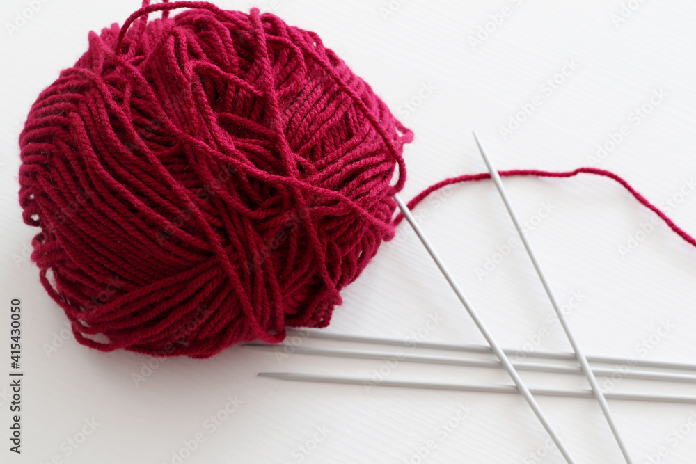 ball of red wool yarn and five knitting needles