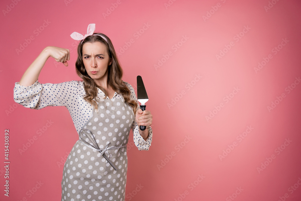 young charming woman pastry chef with a spatula in her hands. A cook in a polka-dot apron. pastry chef in an apron on a pink background. young charming woman pastry chef with a spatula in her hands. A cook in a polka-dot apron. pastry chef in an apron on a pink background.