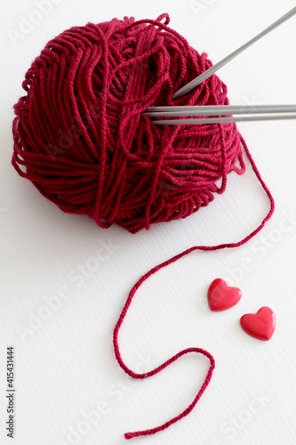 red wool yarn ball with knitting needles and hearts © Iveta