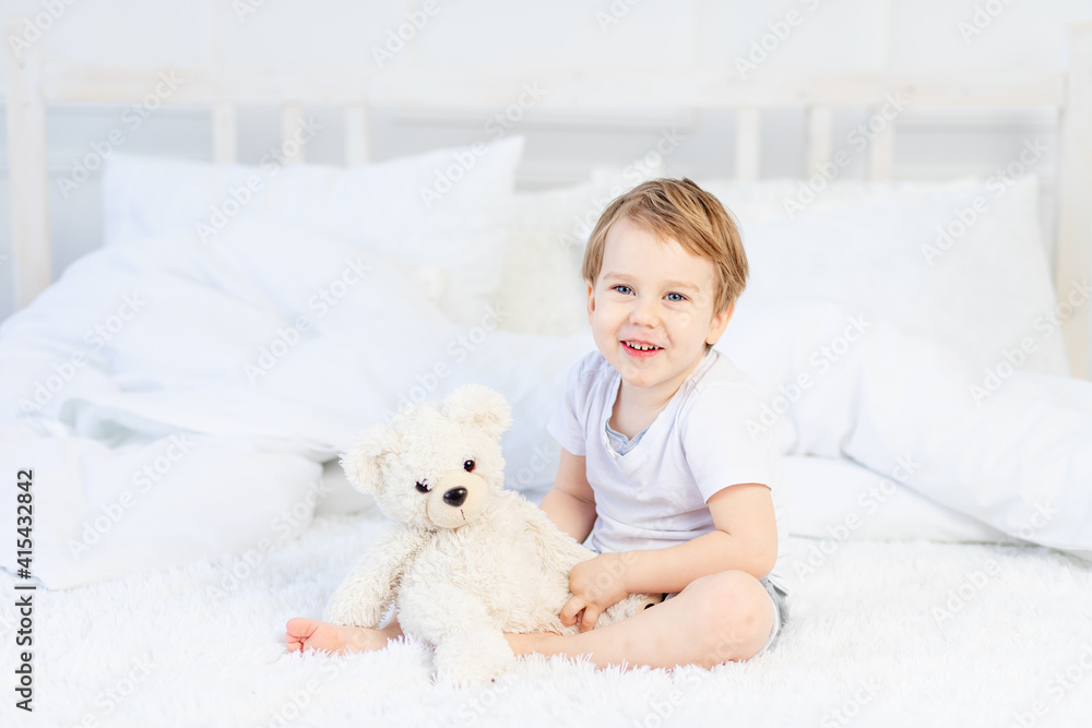 a child with a teddy bear on the bed at home plays and laughs