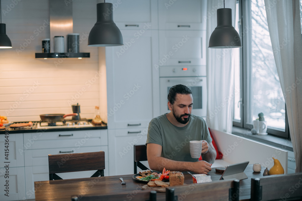 Fototapeta premium A man is having breakfast at home with a tablet.