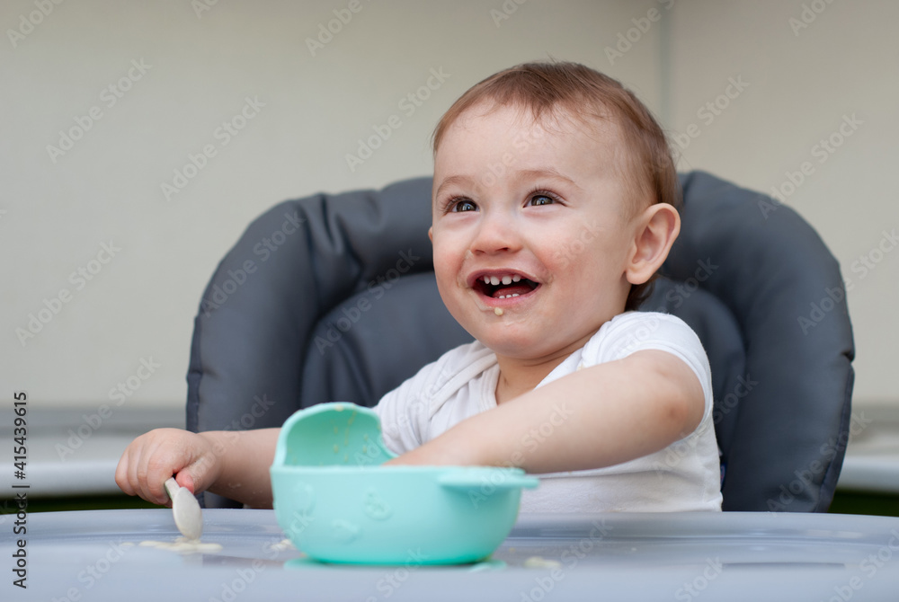 Mother feeding hungry baby in the highchair indoors Mother feeding hungry baby in the highchair indoors