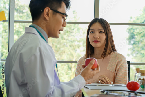 Asian medical doctor wearing stethoscope advising young beautiful patient about healthy diet fruits and virus protection