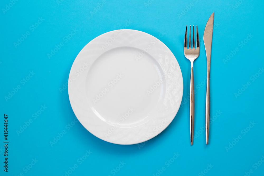 Empty white plate, fork and knife on blue background. Top view. Empty white plate, fork and knife on blue background. Top view.
