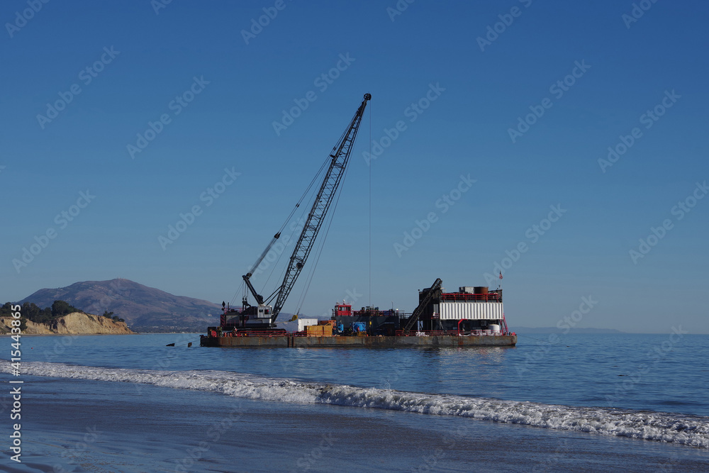 A big barge with work equipment anchored close to an ocean beach to perform oil well work A big barge with work equipment anchored close to an ocean beach to perform oil well work