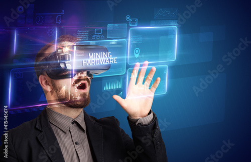 Businessman looking through Virtual Reality glasses with MINING HARDWARE inscription, new technology concept