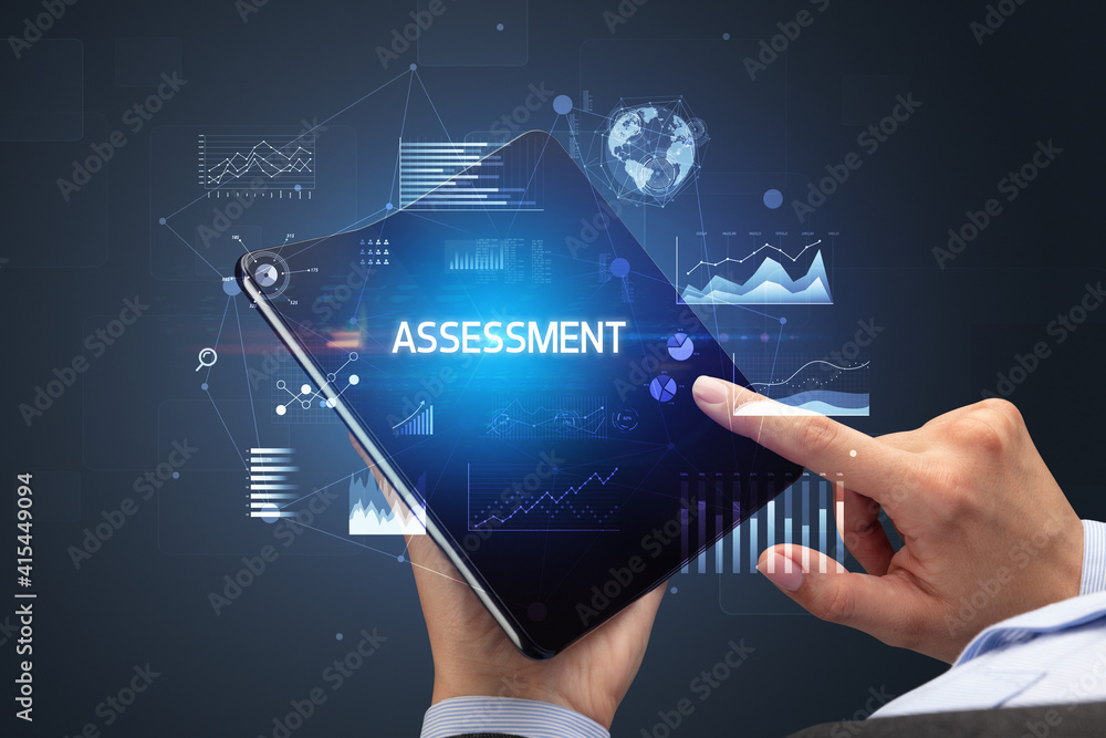 Businessman holding a foldable smartphone with ASSESSMENT inscription, successful business concept Businessman holding a foldable smartphone with ASSESSMENT inscription, successful business concept