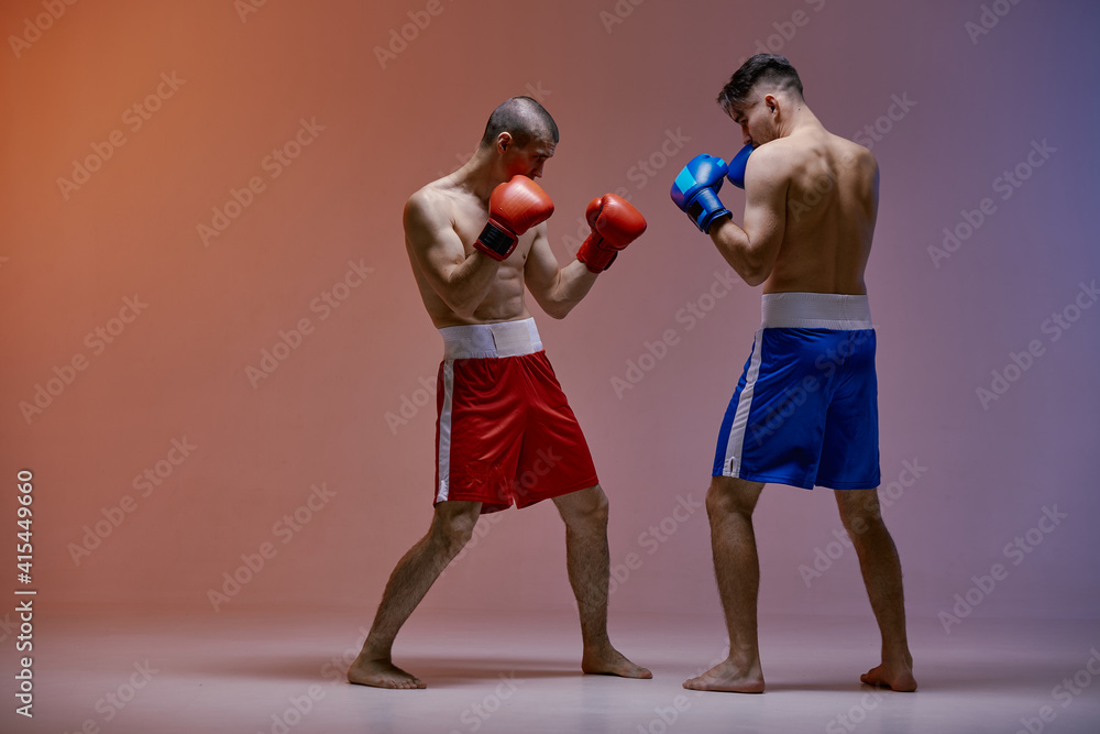 Wrestling of two fighting males boxers standing in stance in red light in studio, martial arts, mixed fight concept