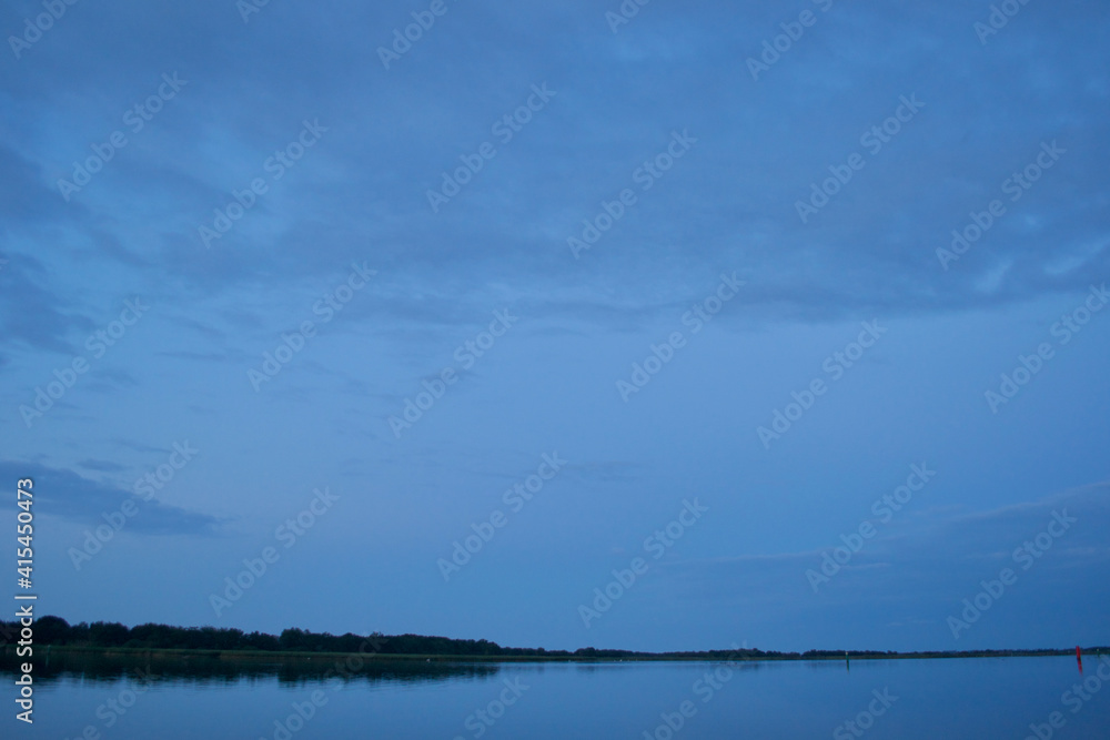 Very blue light in the evening: an enormous tranquil lake, with reflections of the far riverbank