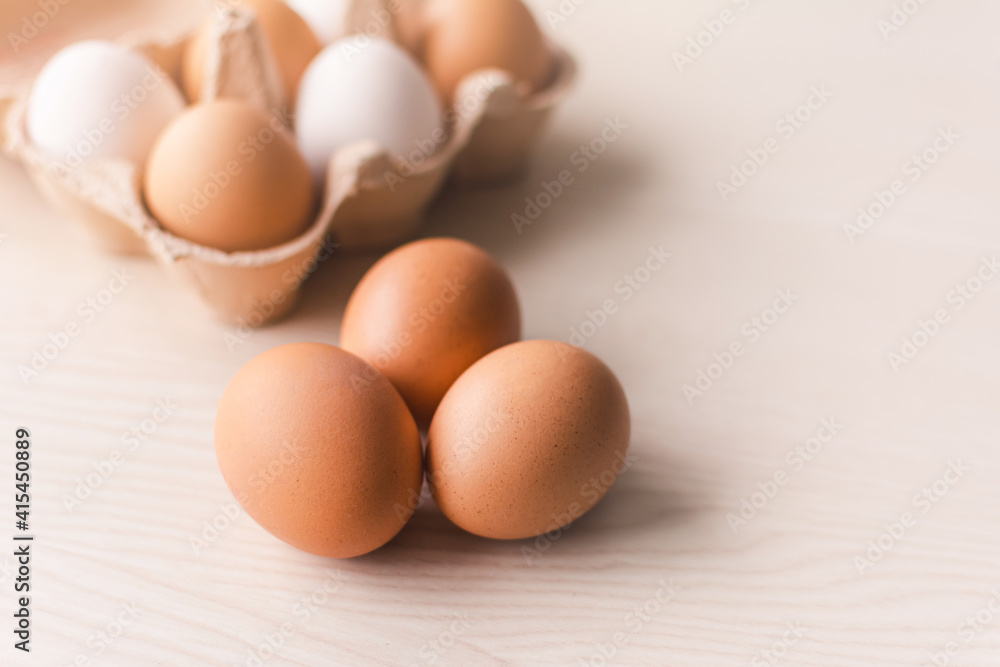 Three raw chicken eggs on a wooden table with a group of eggs in a box on the background.