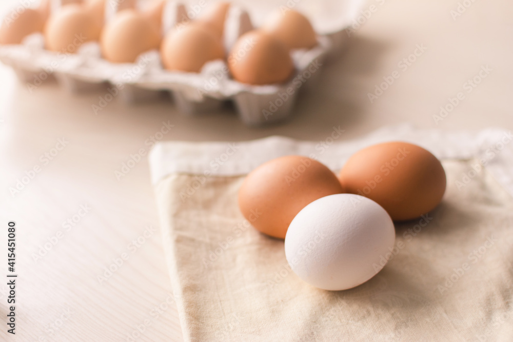 Three raw chicken eggs on a cloth bed with a group of eggs in a box on the background.