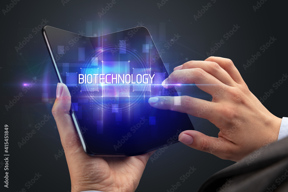 Businessman holding a foldable smartphone with BIOTECHNOLOGY inscription, new technology concept Businessman holding a foldable smartphone with BIOTECHNOLOGY inscription, new technology concept