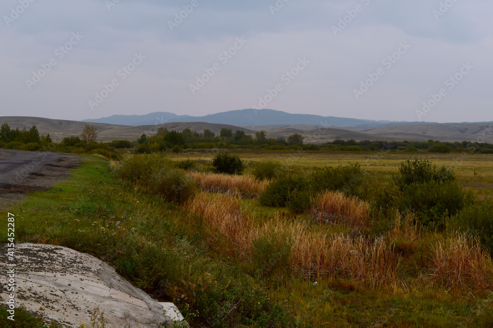 The slope of the road, the meadow, in the distance towering cliffs covered with shrouded mist. The landscape is overcast summer. The slope of the road, the meadow, in the distance towering cliffs covered with shrouded mist. The landscape is overcast summer.