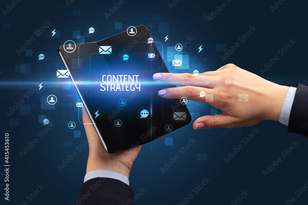 Businessman holding a foldable smartphone with CONTENT STRATEGY inscription, social networking concept Businessman holding a foldable smartphone with CONTENT STRATEGY inscription, social networking concept