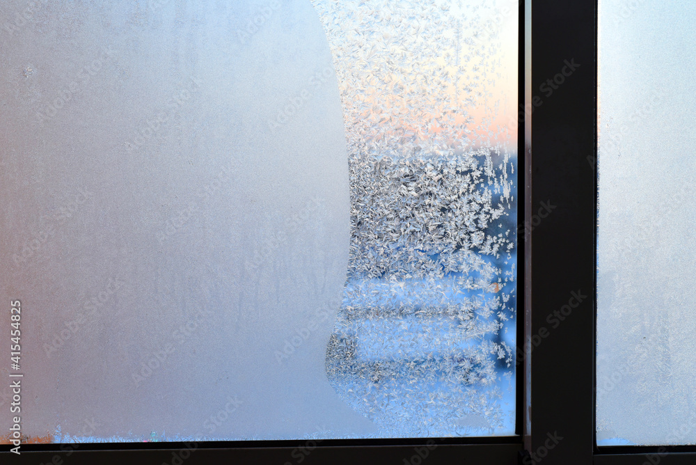 Fototapeta premium Winter. Cold. Frozen window with a beautiful frosty pattern in the form of snowflakes. The pink dawn is visible through the glass.