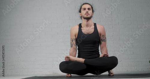 Beautiful young man working out in loft interior, doing yoga exercise on a mat, arm balance exercise with crossed legs, Scale Posture, Tolasana, Utpluthi Pose photo