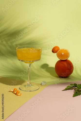 Refreshing Summer juice with ice,fresh orange,lemon and kumquat on green background with hard shadows of palm leaves on background.Balancing citrus fruits and refreshing cocktail.