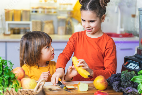 Children cook green smoothies. Kids cut greens: spinach, parsley, Kale and put in Blender. Sisters learn how to prepare a fresh and healthy breakfast