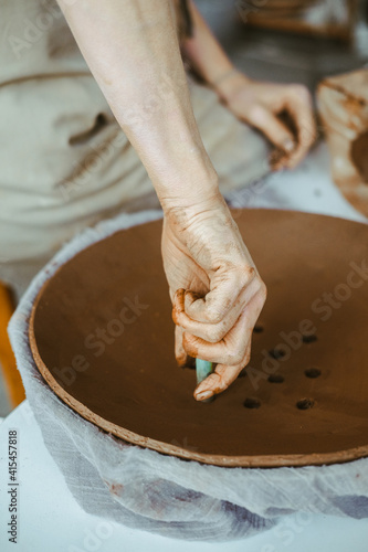 A woman's hands work with clay. Dirty fingers create a plate photo