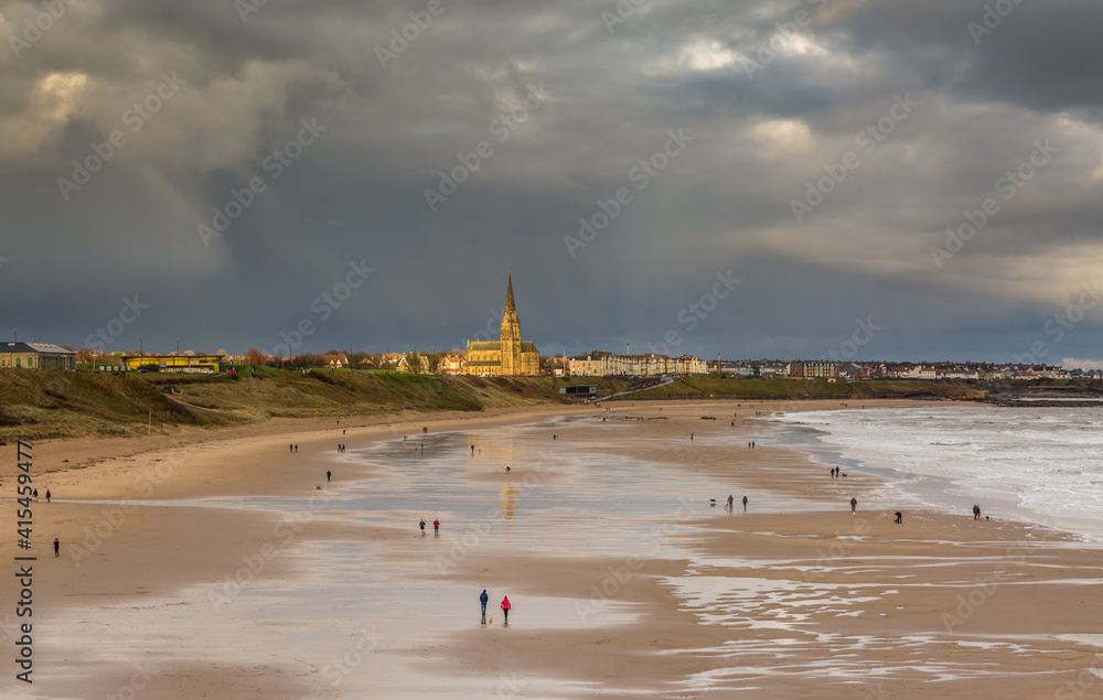 Fototapeta premium People taking a walk on Tynemouth's Longsands beach during Lockdown on a cloudy and rainy day, in the north east of England