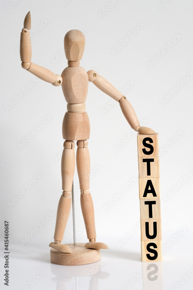 The wooden man raised his hand, and under his left hand he has cubes with the inscription - STATUS The wooden man raised his hand, and under his left hand he has cubes with the inscription - STATUS