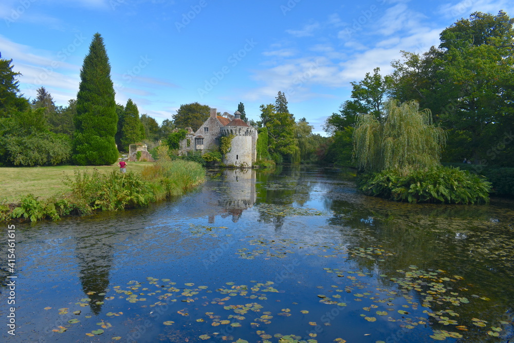 A woman admiring the exterior of a British medieval castle and its reflection in water Exotic gardens with panoramic views of a moated fortress and a Victorian country mansion all in a historic estate