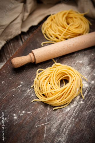 Uncooked fresh spaghetti nests on a wooden table with a rolling pin. Italian pasta homemade. Text space