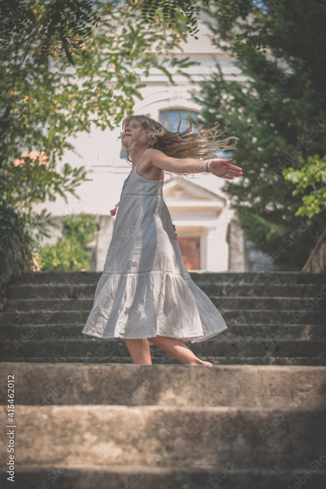 happy child dancing outdoors free in stairs with long hair blowing in the wind in sunny summer day