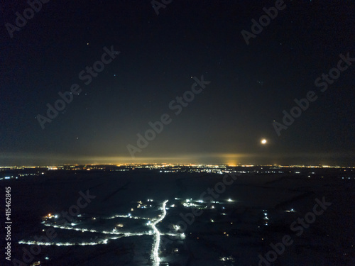 Distant lights of the night city under the starry sky. Aerial drone view. Winter frosty night.