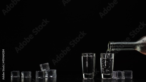 Two hands with glasses of vodka making cheers on black background with ice cubes. Celebration of business success, Christmas, anniversary, birthday. Raising toast with glasses of tequila or sake