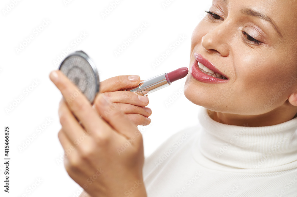 Closeup of a young woman with beautiful smile applying a lipstick on her lips and looking at herself at a small cosmetic mirror Closeup of a young woman with beautiful smile applying a lipstick on her lips and looking at herself at a small cosmetic mirror