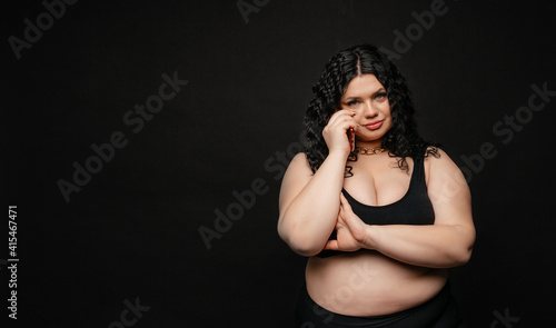 Plus size model in lingerie, fat sexy woman in underwear on black studio background, body positive concept, full length portrait. Girl model plus size talking on the phone