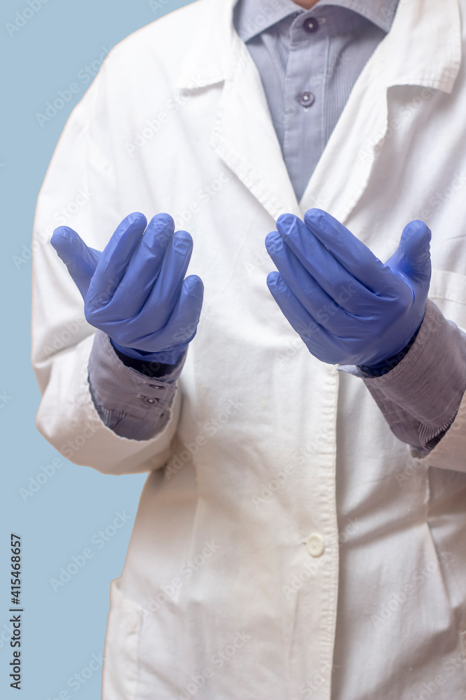 A young man in a white medical coat raised his hands and prayed. Medical gloves. Blue background. The doctor is praying. A Muslim makes dua A young man in a white medical coat raised his hands and prayed. Medical gloves. Blue background. The doctor is praying. A Muslim makes dua