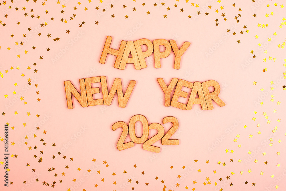 Obraz premium Funny Christmas inscription happy new year 2022 in wooden letters on a pink background with gold stars.