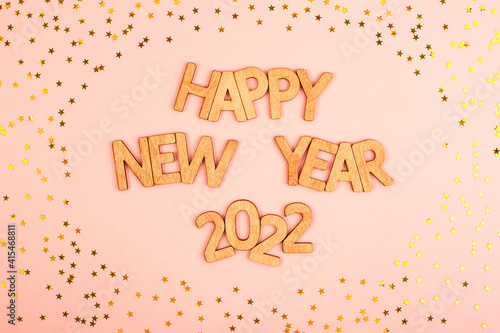 Funny Christmas inscription happy new year 2022 in wooden letters on a pink background with gold stars.