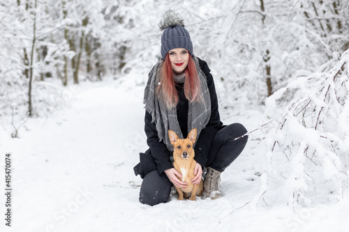 Smiling beautiful girl is posing with her brown dog in wintry snowy nature.