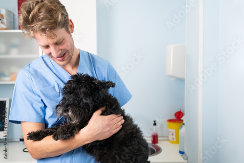 Young male veterinarian doctor with stethoscope holding and examining cute dog at veterinary clinic. Pet health care and medical concept. High quality photo